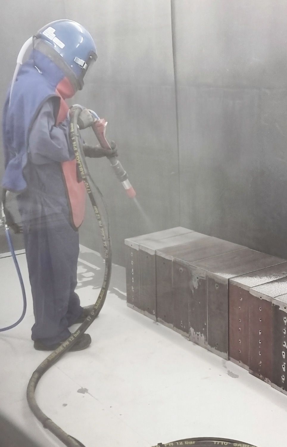 Ouvrier en cabine effectuant le sablage de pièces métalliques avant application du thermolaquage - Division « Bâtiment » de Creusalp SA